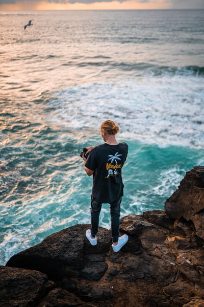 男孩蓝色的水手领t恤站在岩石附近海白天
